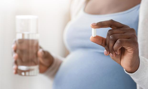 A pregnant woman holding a glass of water and a pill.